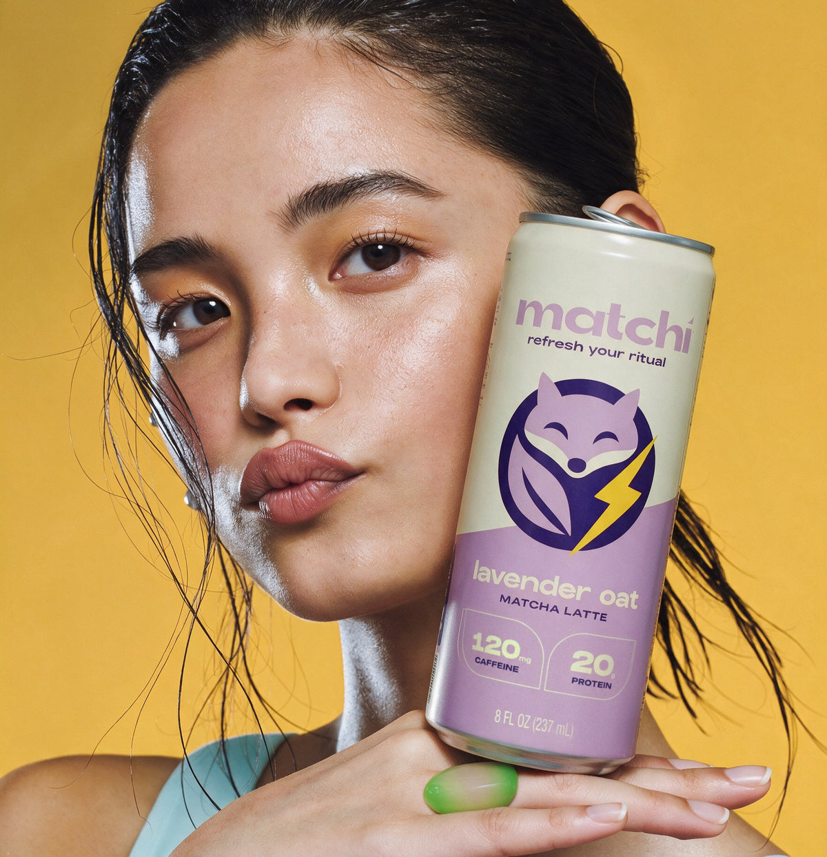 A woman holds a Matchi Lavender Oat can beside her face on a mustard backdrop