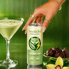 MATCHI vanilla oat matcha latte can held by a hand with gold rings, next to a martini glass of matcha and chocolates.